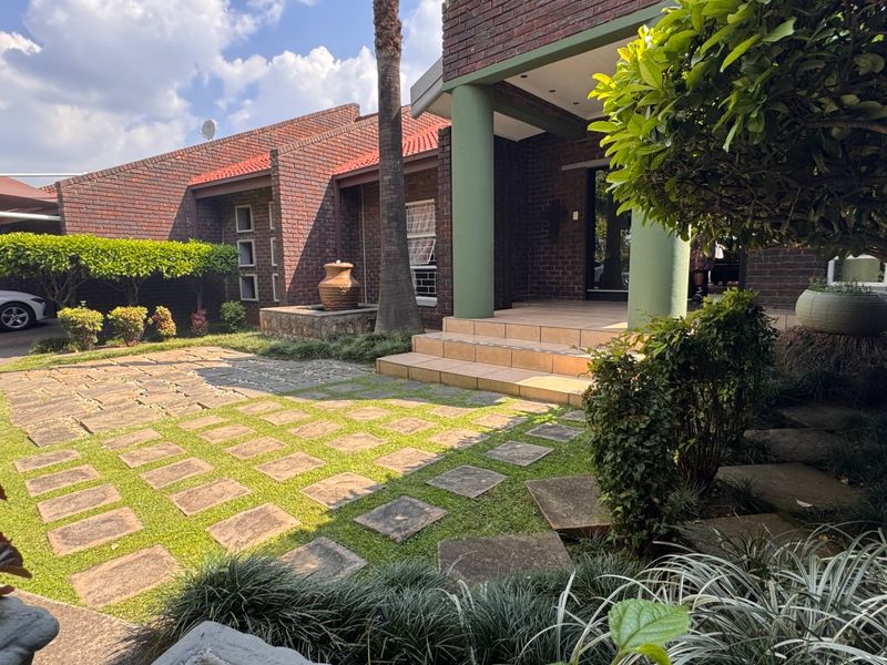 A well-maintained front entrance featuring a brick facade, covered porch with tiled steps, and a landscaped garden with stone paver pathways.