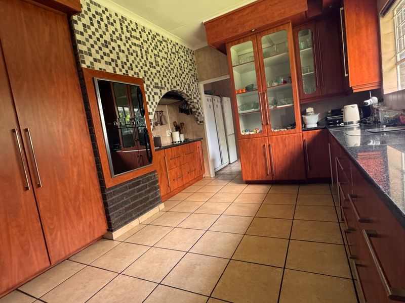A spacious kitchen featuring warm-toned wooden cabinetry, granite countertops, tiled flooring, and a unique brick and mosaic tile feature wall.