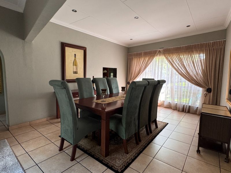 A well-maintained dining room featuring neutral wall tones, tiled flooring, and large windows with curtain treatments, providing a comfortable space for formal dining.