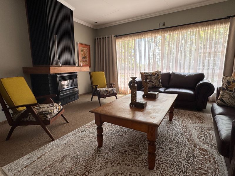 A comfortable living room featuring a prominent fireplace with a timber mantelpiece and vertical slat detailing, complemented by a large window.