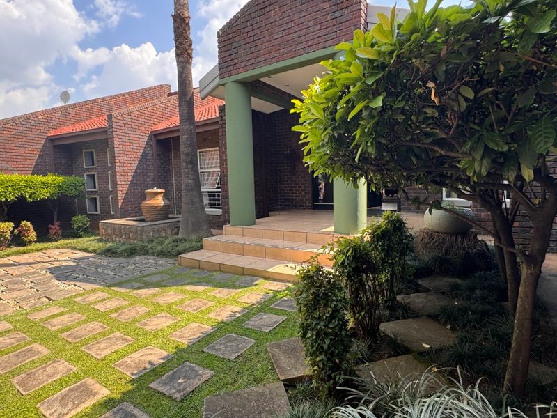 A well-maintained face brick home entrance featuring a paved front garden, tiled steps, and structural columns under a tiled roof.