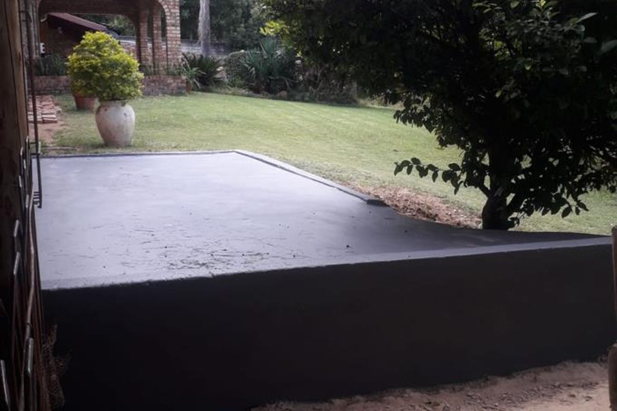 Rear exterior view featuring a newly painted concrete patio slab, adjacent garden area, and a brick-built covered patio structure in the background.