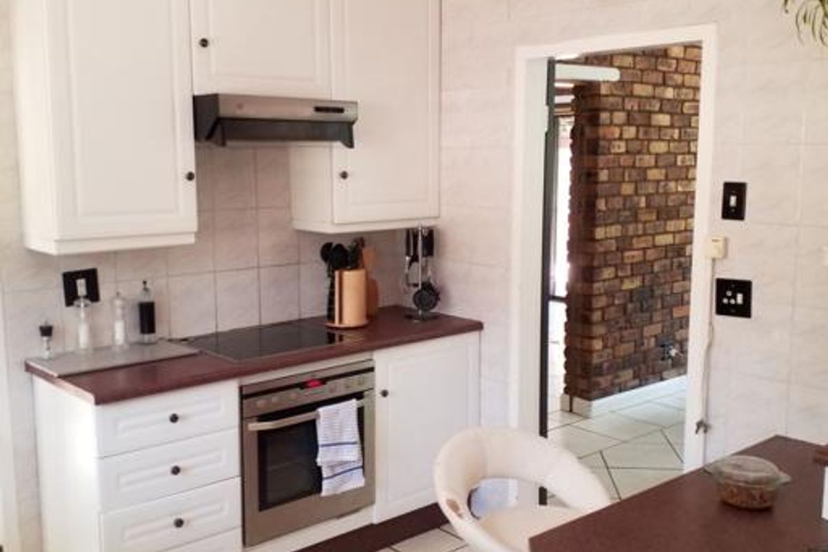 A functional kitchen featuring white cabinetry, a built-in oven with hob, extractor fan, and tiled flooring, leading into an adjacent living area.