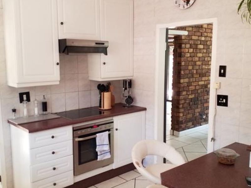 A functional kitchen featuring white cabinetry, a built-in oven with hob, extractor fan, and tiled flooring, leading into an adjacent living area.