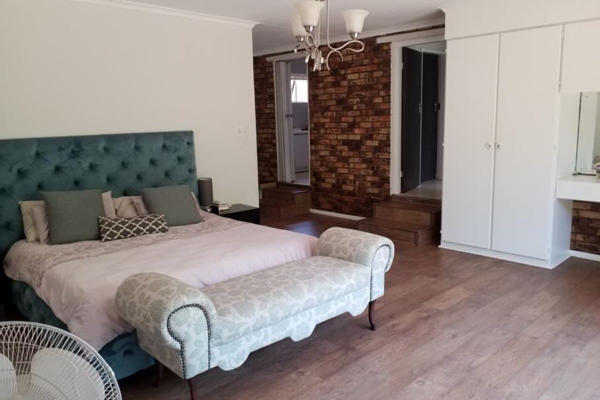Spacious bedroom featuring an exposed brick wall, built-in cupboards, and laminate flooring with a stepped transition to the adjacent area.