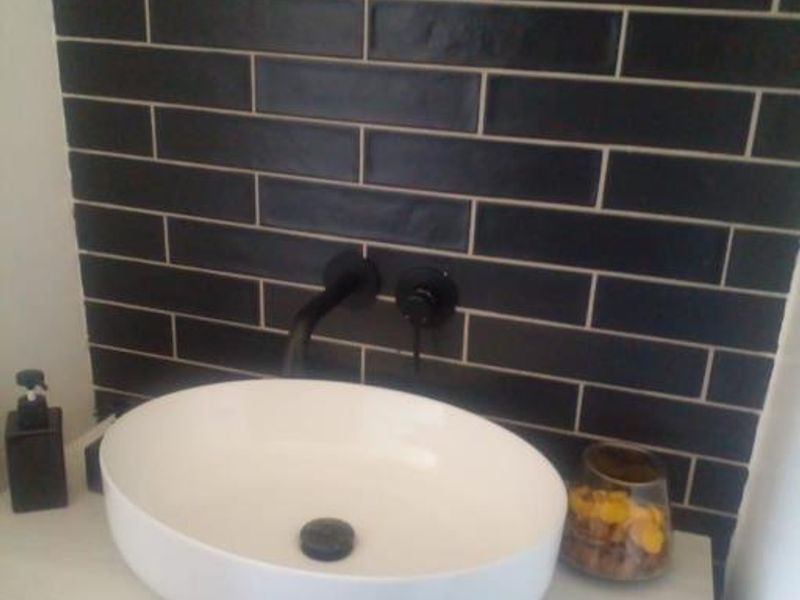 Modern bathroom vanity featuring a white vessel sink, matte black wall-mounted faucet, and stylish dark subway tile backsplash.