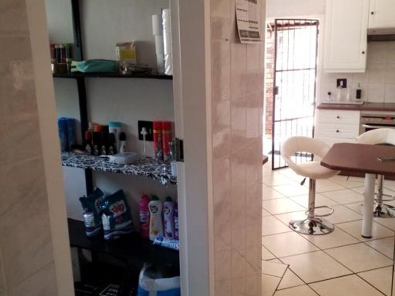 A functional scullery area with built-in shelving, adjacent to a tiled kitchen space featuring white cabinetry and a security gate.