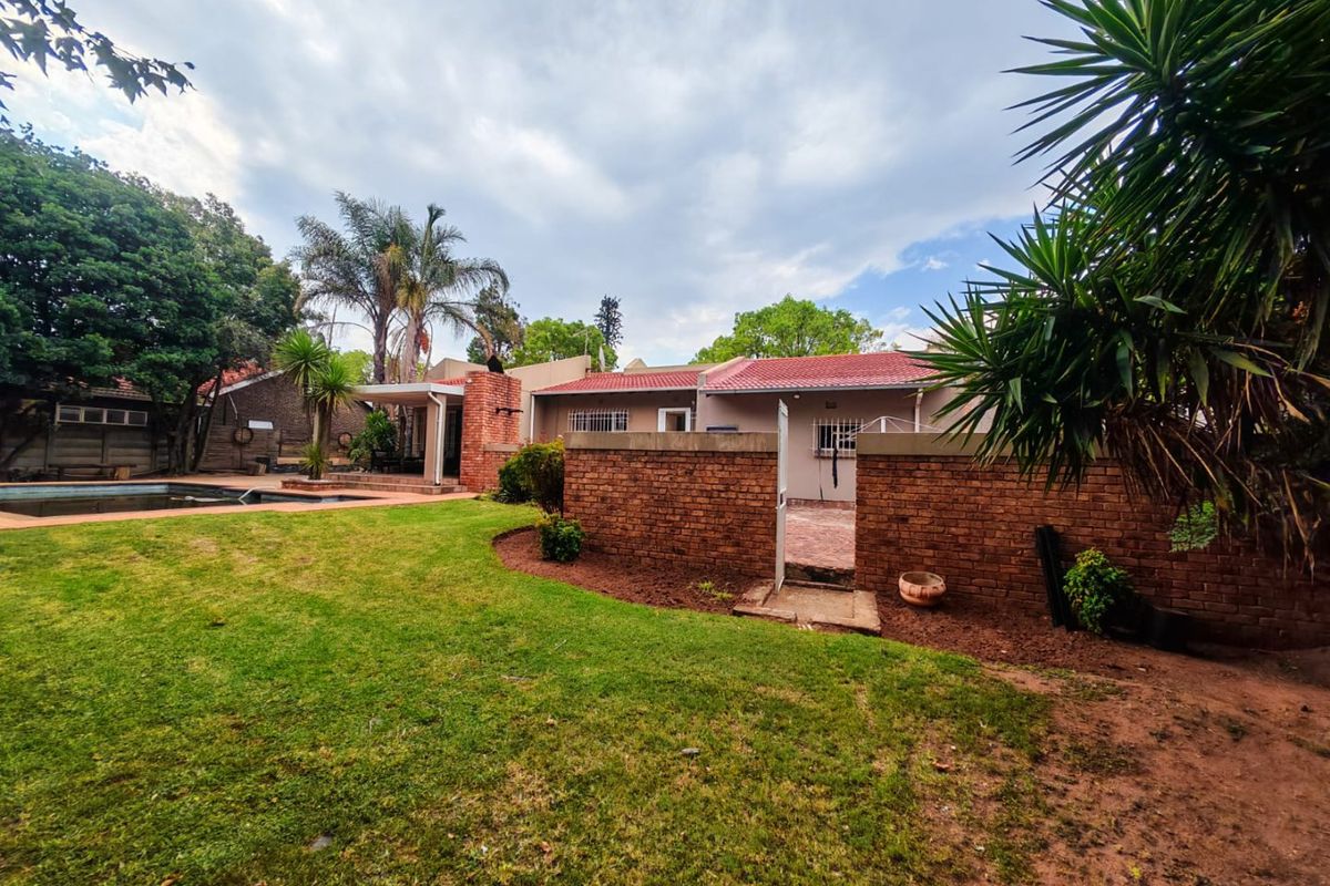 Rear view of the property featuring a swimming pool, covered patio area, and a private garden enclosed by a brick boundary wall.