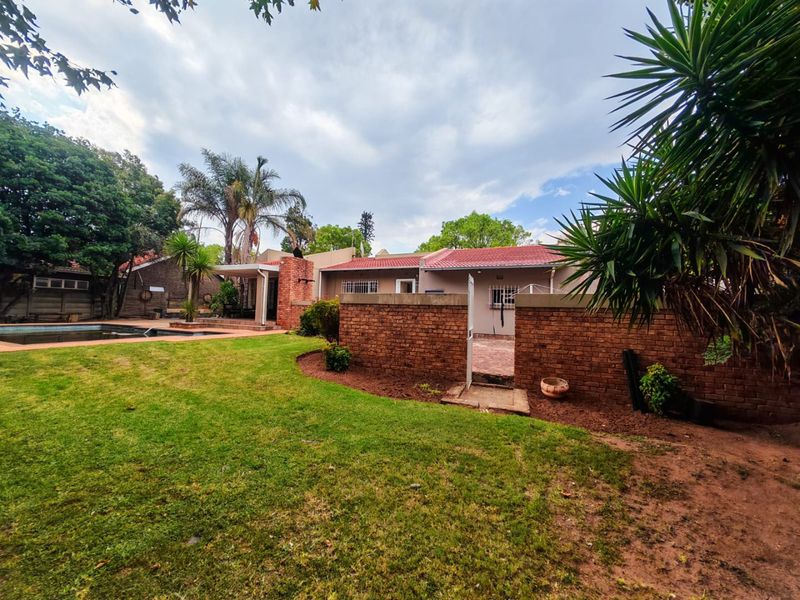 Rear view of the property featuring a swimming pool, covered patio area, and a private garden enclosed by a brick boundary wall.