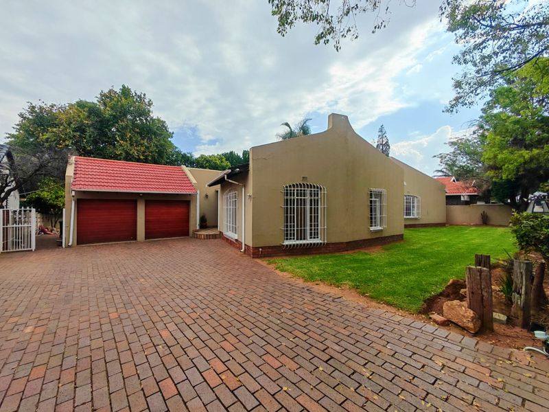 Front view of a house featuring a double garage, brick paved driveway, and well-maintained lawn with security bars on windows.