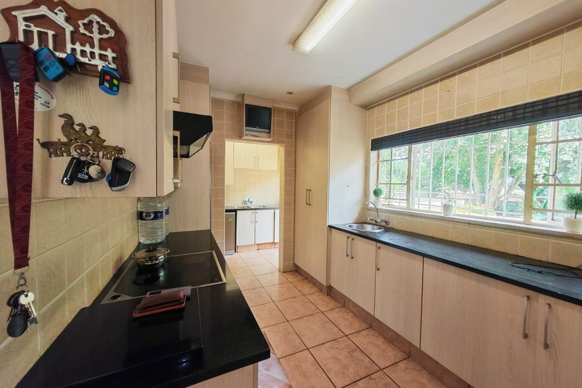 Functional kitchen featuring light wood-finish cabinetry, dark countertops, tiled flooring, and a scullery area visible through the doorway.