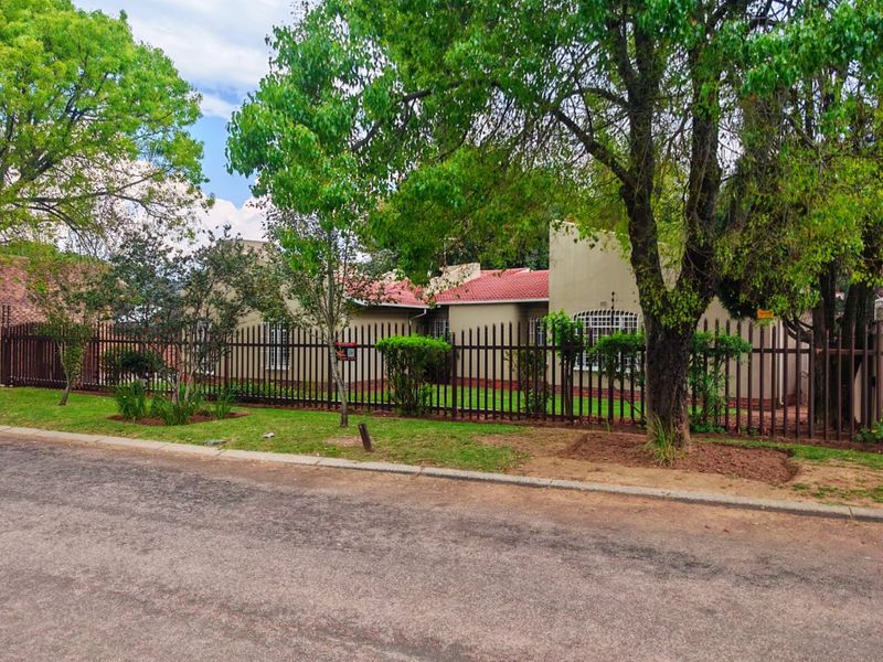 Front view of a single-story residential property featuring a tiled roof, security fencing, and established garden trees.
