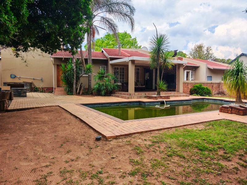 Rear exterior view featuring a swimming pool, covered patio area, and brick paving, set against a residential house with a tiled roof.