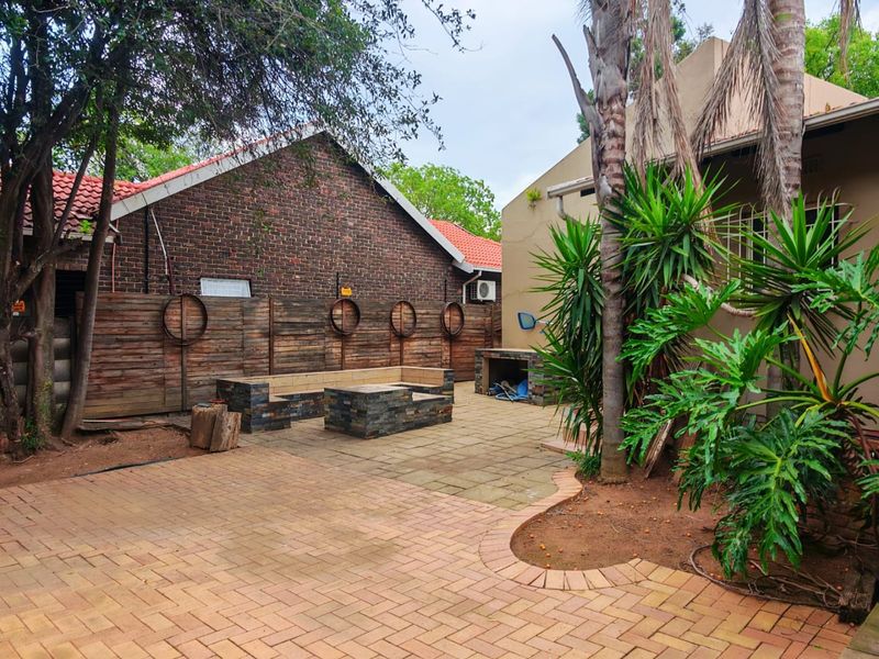 Outdoor patio area featuring a built-in braai, stone-clad seating, and paved flooring, surrounded by established garden greenery and a timber boundary fence.