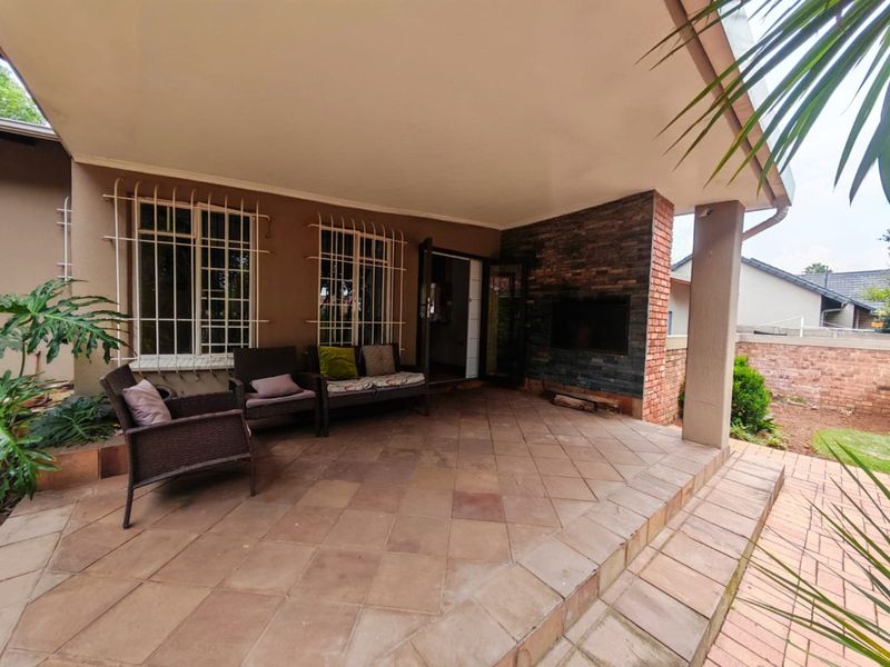 A covered patio area featuring tiled flooring, a built-in fireplace with stone cladding, and security bars on the windows.