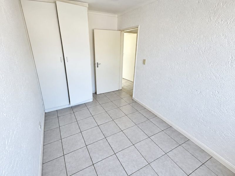 A clean, empty bedroom featuring neutral tiled flooring and built-in cupboards, offering a blank canvas for personalization.