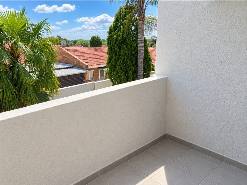 A clean, minimalist balcony featuring tiled flooring and a solid masonry balustrade, offering an open view of the surrounding neighborhood.