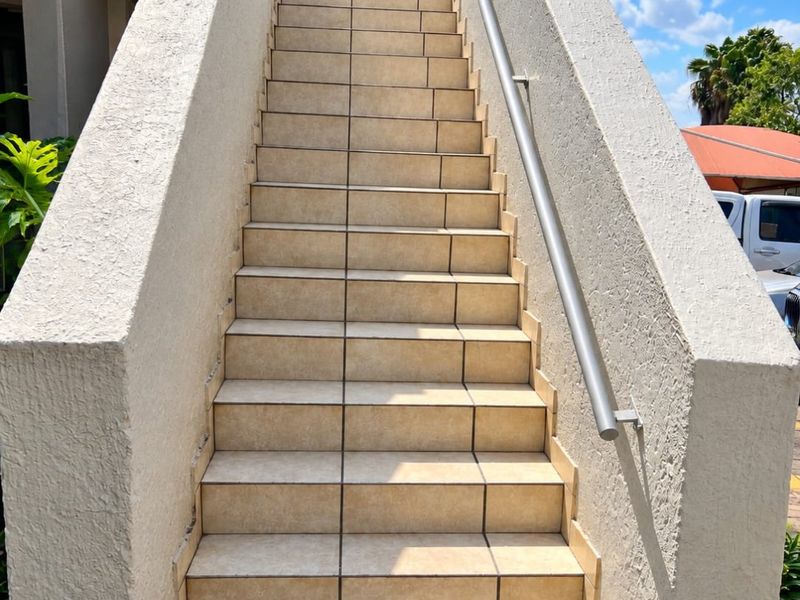 An exterior staircase featuring tiled steps and a metal handrail, providing access to the apartment entrance.