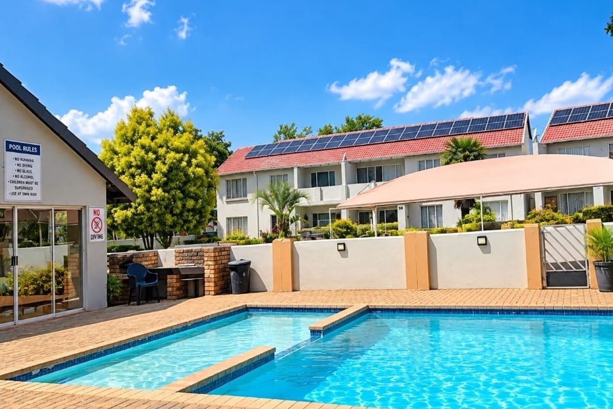 Communal swimming pool area featuring brick paving, a built-in braai, and a shade sail, set within a well-maintained apartment complex with solar panels.