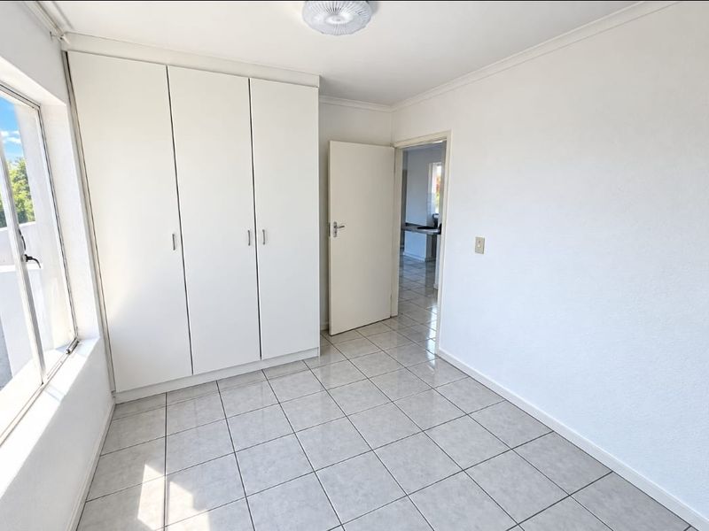 A bright, empty bedroom featuring neutral tiled flooring and ample built-in cupboard storage, offering a clean and versatile space.