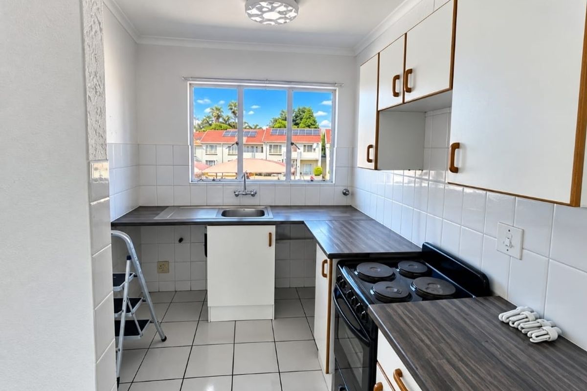 A functional kitchen featuring white cabinetry, dark laminate countertops, a built-in electric stove, and tiled finishes, offering a clean and practical workspace.