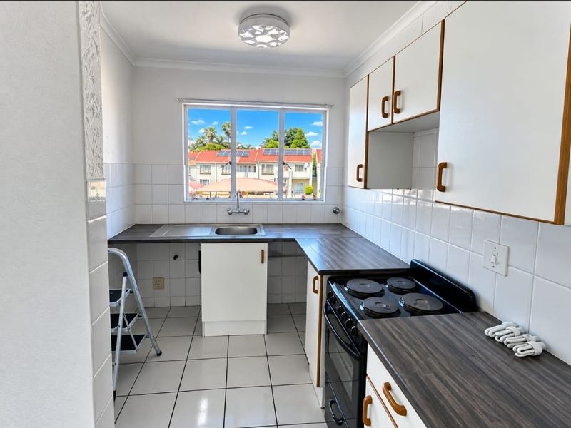 A functional kitchen featuring white cabinetry, dark laminate countertops, a built-in electric stove, and tiled finishes, offering a clean and practical workspace.