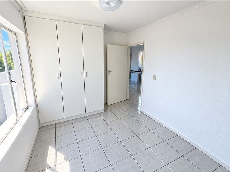 A bright, empty bedroom featuring neutral tiled flooring and ample built-in cupboard storage, offering a clean canvas for personalization.