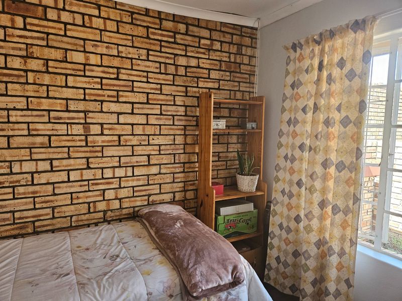 A bedroom featuring a prominent exposed brick feature wall and a window fitted with security bars.