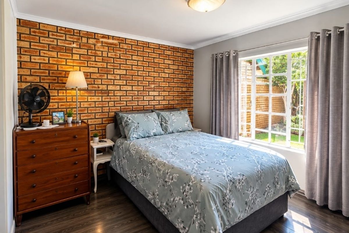A well-maintained bedroom featuring an exposed brick accent wall, laminate flooring, and a window overlooking the garden.