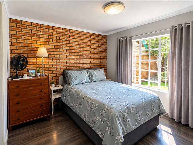 A well-maintained bedroom featuring an exposed brick accent wall, laminate flooring, and a window overlooking the garden.