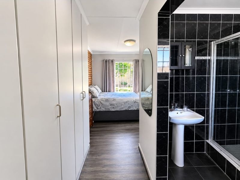 Bedroom featuring built-in cupboards, laminate flooring, and an en-suite bathroom with a pedestal basin and shower enclosure.