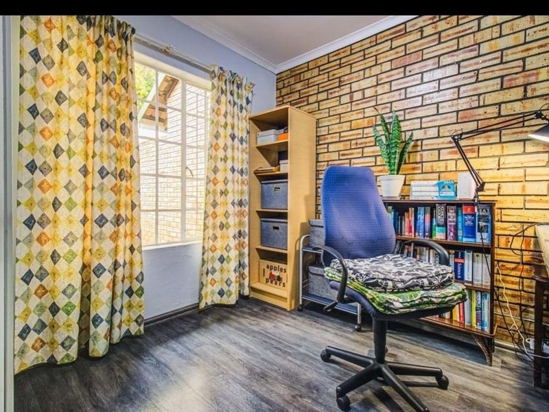 A functional home office featuring an exposed brick feature wall, laminate flooring, and natural light from a window with security bars.