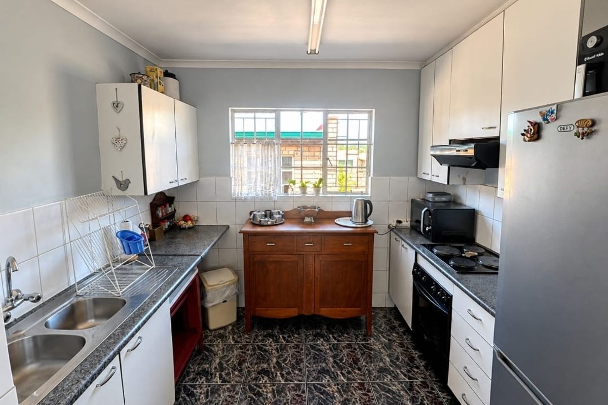 A functional kitchen featuring white cabinetry, laminate countertops, a double basin sink, and built-in electric cooking appliances with tiled splashbacks.