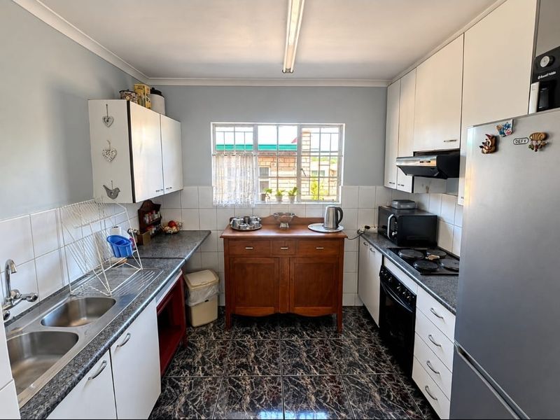 A functional kitchen featuring white cabinetry, laminate countertops, a double basin sink, and built-in electric cooking appliances with tiled splashbacks.