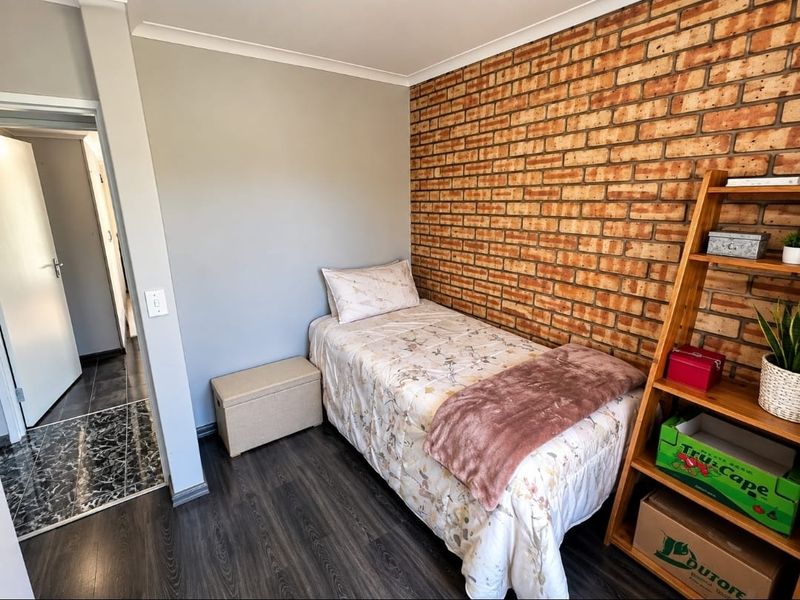 A cozy bedroom featuring a distinctive exposed brick feature wall, modern laminate flooring, and neutral wall finishes.