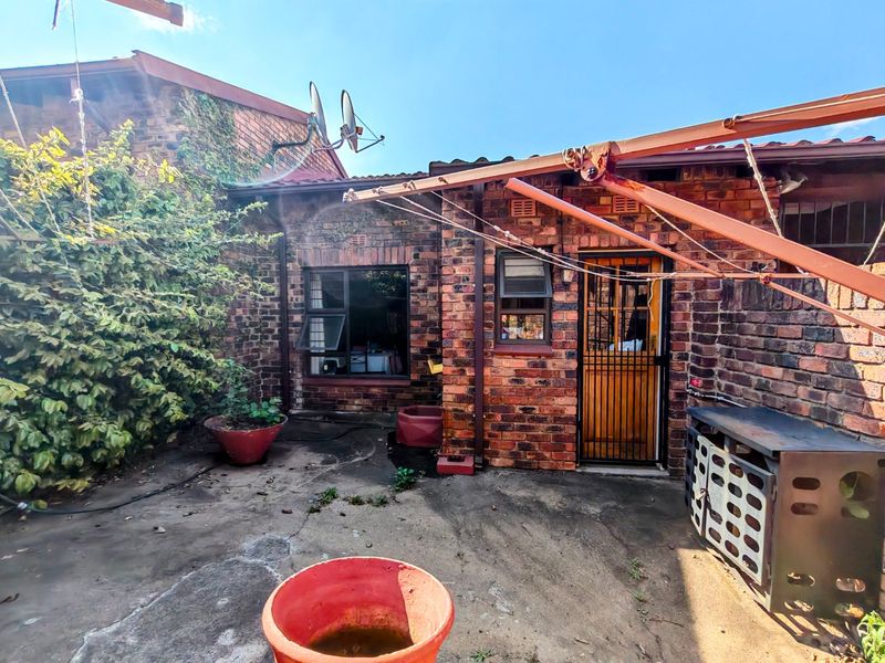 Rear exterior area featuring a brick facade, concrete patio, and security gate access, providing a functional outdoor space with potential for landscaping improvements.