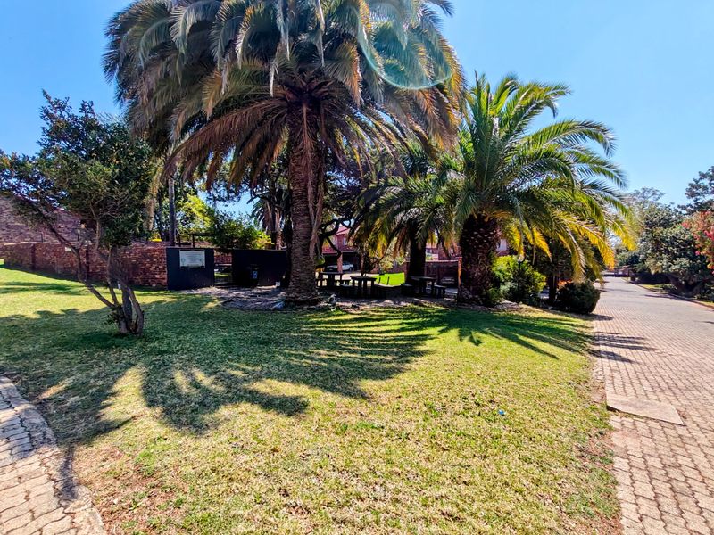 A well-maintained communal garden area featuring mature palm trees, manicured lawn, and paved pathways within the townhouse complex.