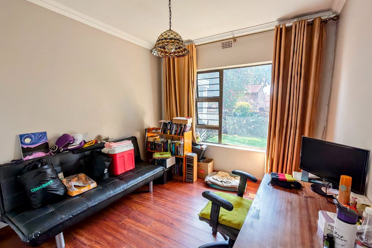 A bedroom featuring laminate flooring, a steel frame window, and a decorative pendant light fixture, offering a functional space with natural light.