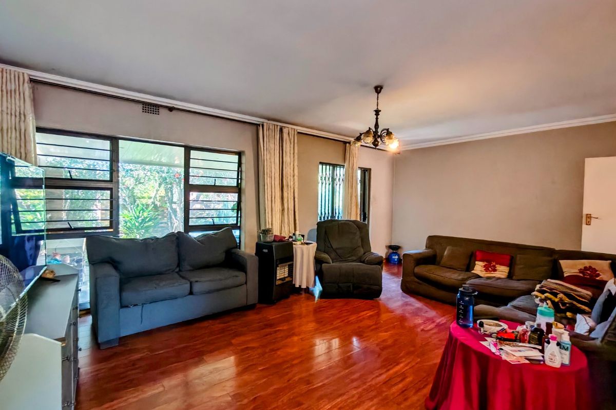 Spacious living room featuring warm-toned laminated timber flooring, large windows with security bars, and classic ceiling cornice detailing.