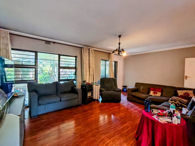 Spacious living room featuring warm-toned laminated timber flooring, large windows with security bars, and classic ceiling cornice detailing.