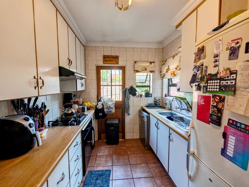 A functional galley-style kitchen featuring built-in cabinetry, a gas hob, an extractor fan, and tiled finishes with direct access to the rear exterior.