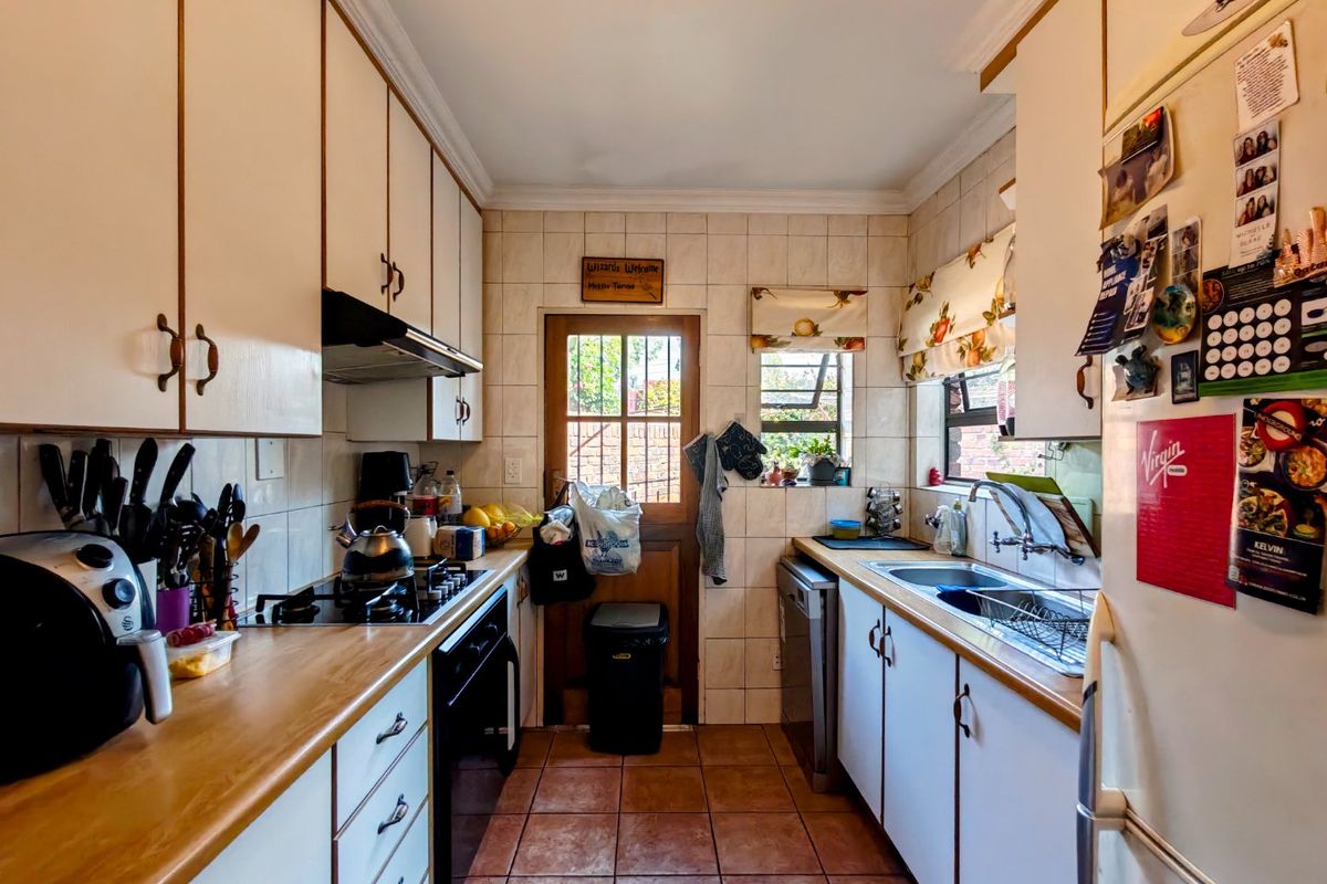 A functional galley-style kitchen featuring built-in cabinetry, laminate countertops, a gas hob, and direct access to the rear exterior.