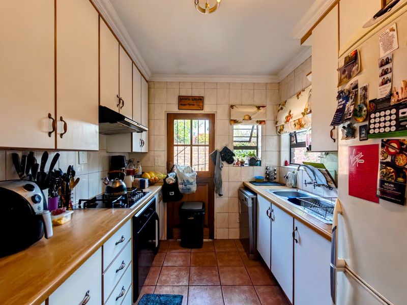 A functional galley-style kitchen featuring built-in cabinetry, laminate countertops, a gas hob, and direct access to the rear exterior.