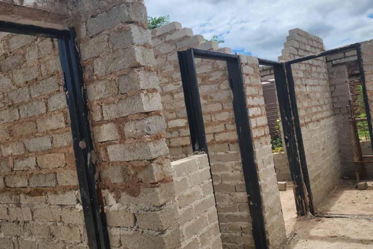 An unfinished construction site showing exposed brick walls and installed steel door frames in an open-air setting.