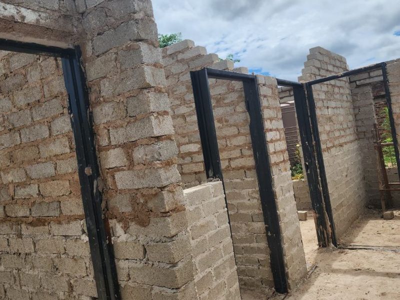 An unfinished construction site showing exposed brick walls and installed steel door frames in an open-air setting.