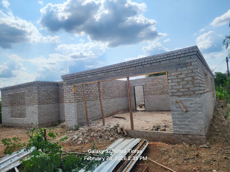 A residential property under construction showing unfinished brick masonry walls, structural lintels, and open door and window frames.