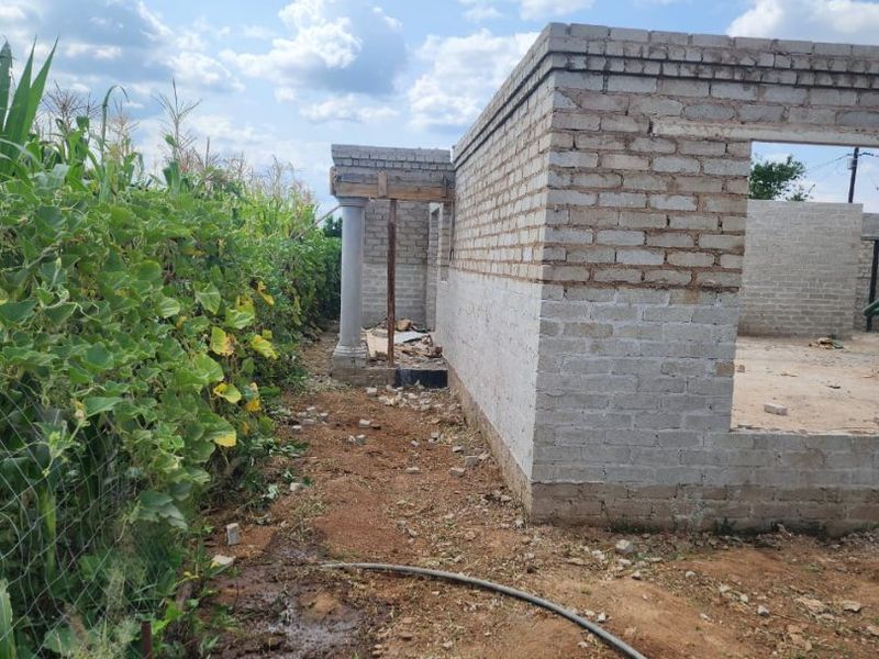 An exterior view of a house under construction, featuring exposed brick walls and a concrete support column in a rural setting.