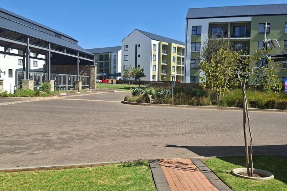 A view of the apartment complex entrance featuring paved driveways, landscaped garden areas, and modern multi-story residential buildings.