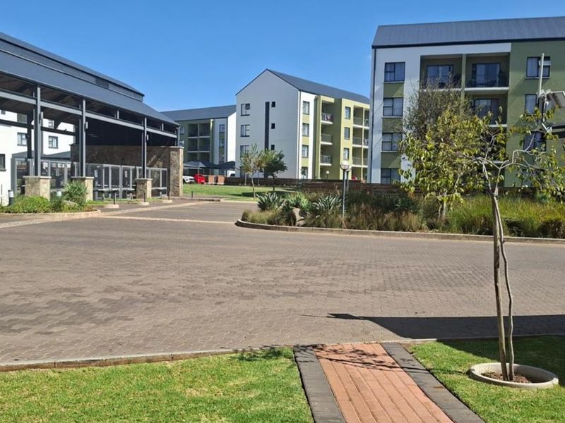 A view of the apartment complex grounds featuring paved driveways, landscaped gardens, and modern multi-story residential buildings.