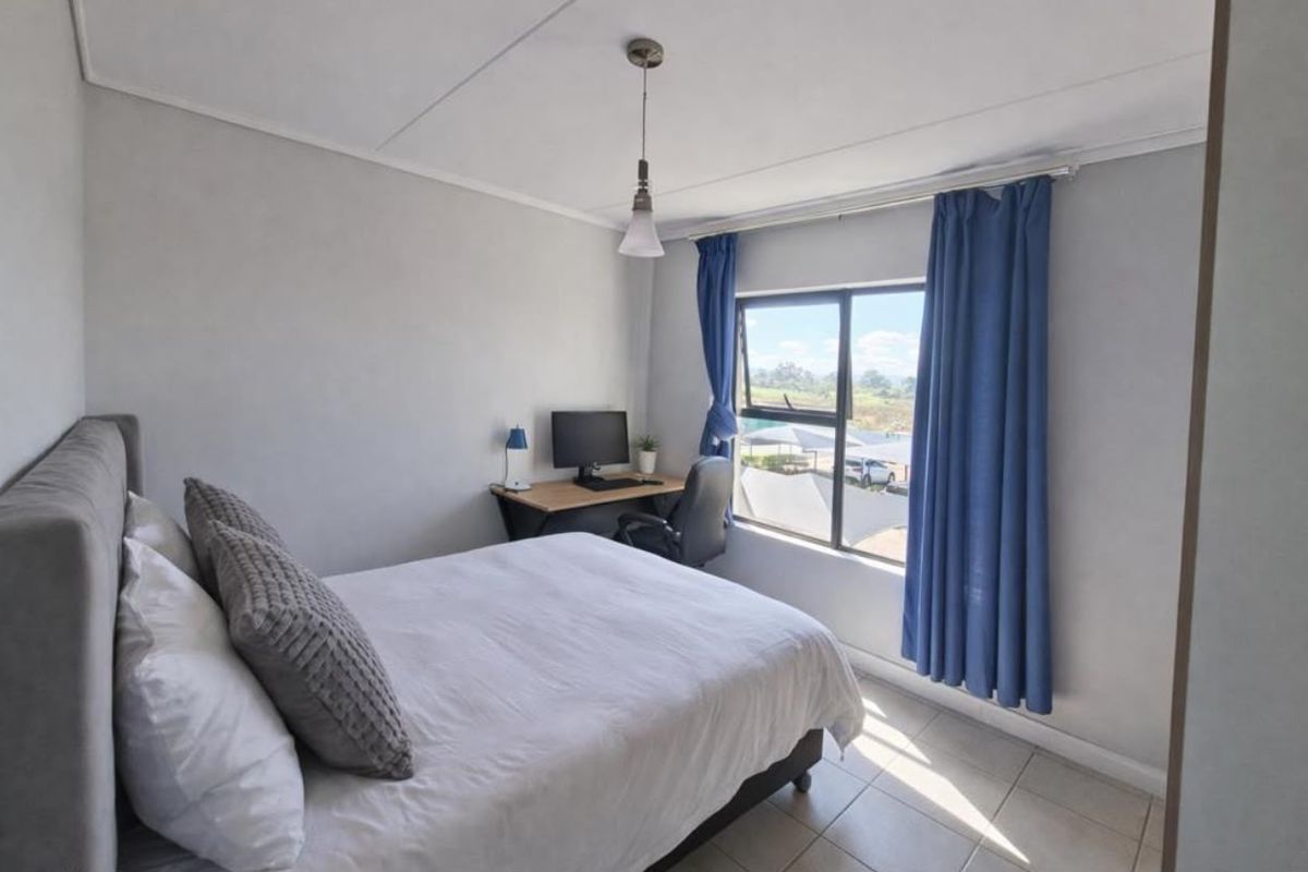 A bright bedroom featuring tiled flooring, a pendant light, and an aluminium window frame with views of the surrounding area.